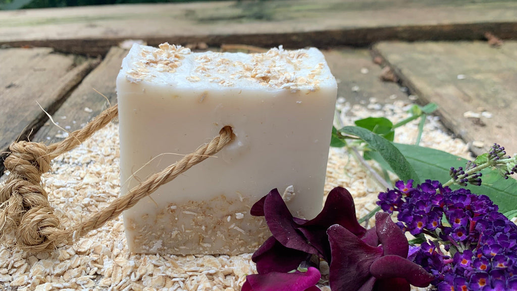 Manchester Candle Makers.Bar of soap with a rope on a wooden surface with purple flowers in the background